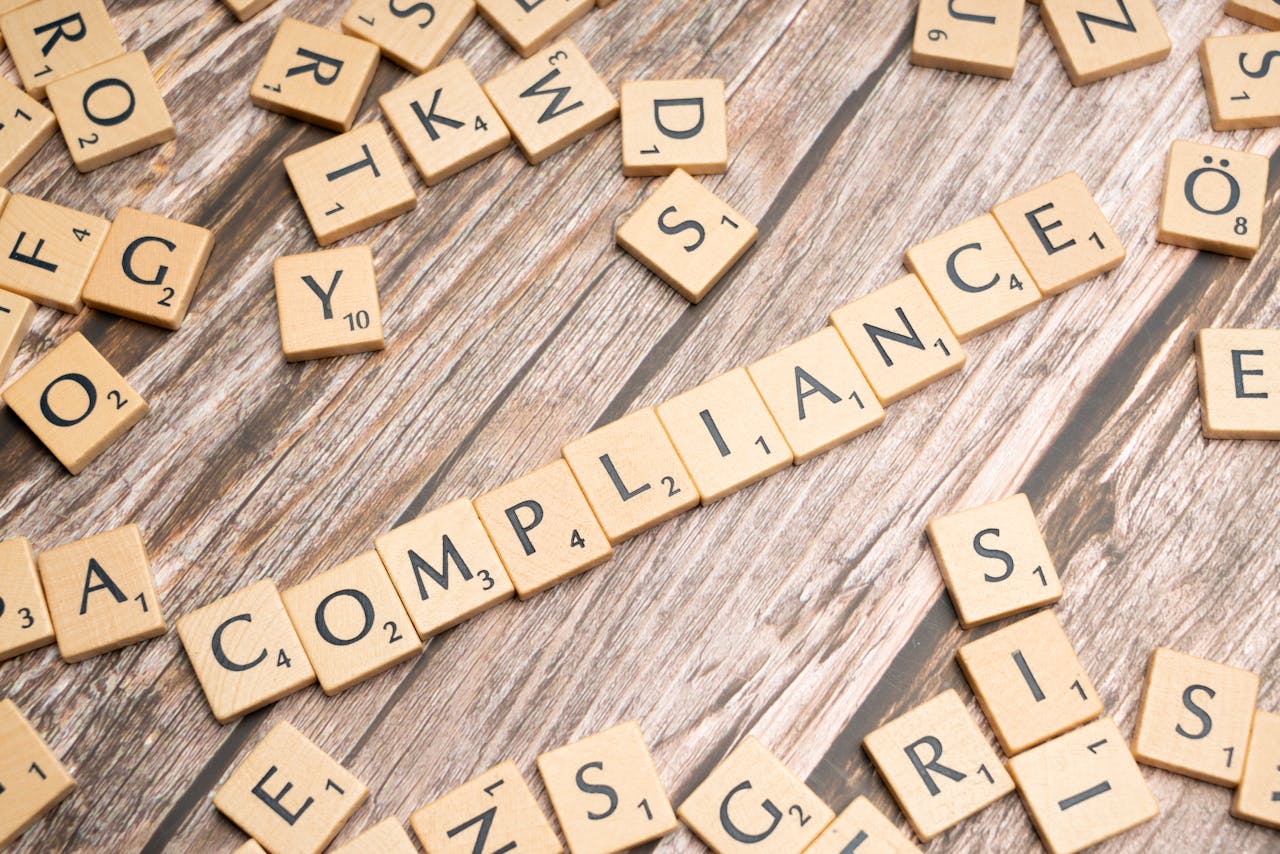 Wooden letter tiles forming the word COMPLIANCE on a rustic wooden background.